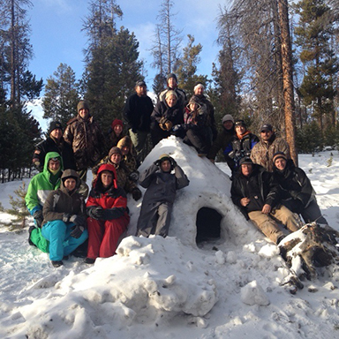 2014 Winter Survival Clinic participants shown near the snow shelter they made
