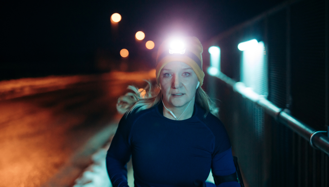 Woman with head lamp on jogging towards camera during winter season