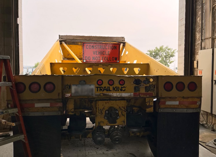 A yellow construction vehicle displays an orange “construction vehicle: Do not follow” sign on the back window.