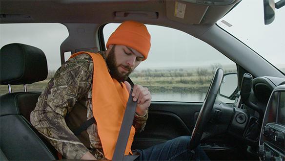 man in hunter orange putting on seatbelt